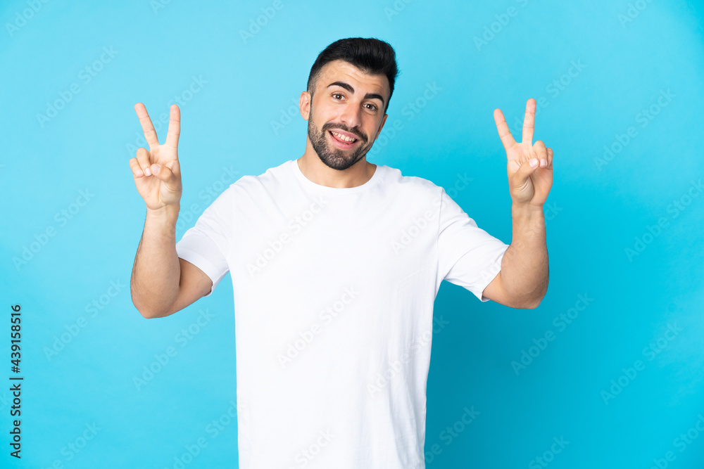Caucasian man over isolated blue background showing victory sign with both hands Caucasian man over isolated blue background showing victory sign with both hands