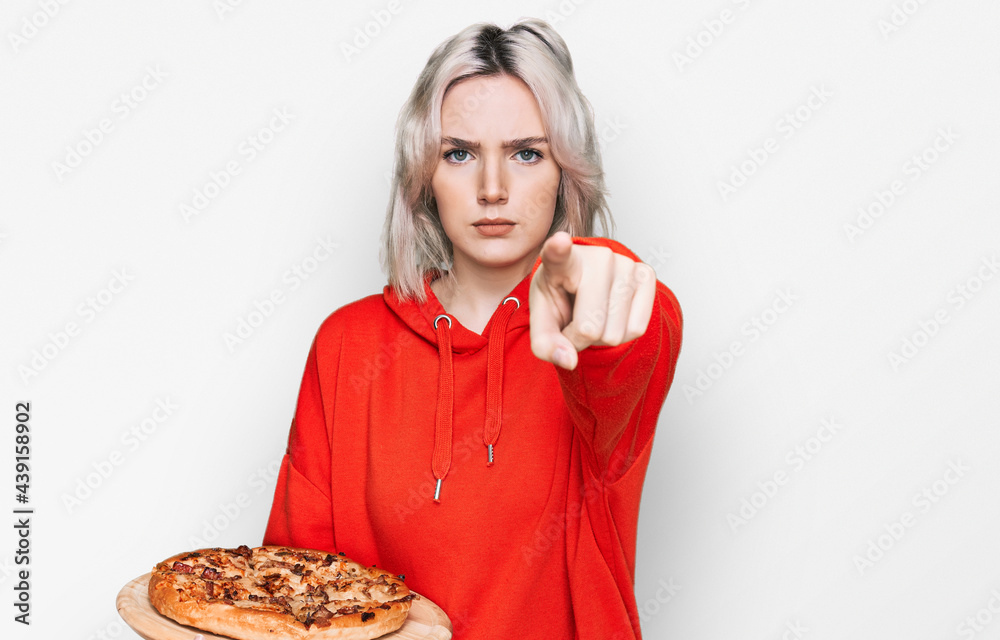 Young blonde girl holding italian pizza pointing with finger to the camera and to you, confident gesture looking serious Young blonde girl holding italian pizza pointing with finger to the camera and to you, confident gesture looking serious