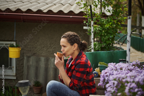 Beautiful mature woman gardener drinking hot drink resting outside the country house photo