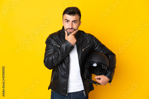 Caucasian man with a motorcycle helmet over isolated yellow background thinking