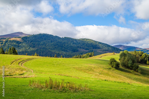 hills covered with grass with a country road on a background of mountains and trees with a blue sky with clouds. Beautiful landscape. © robertuzhbt89