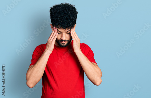 Young arab man with beard wearing casual red t shirt with hand on head for pain in head because stress. suffering migraine.