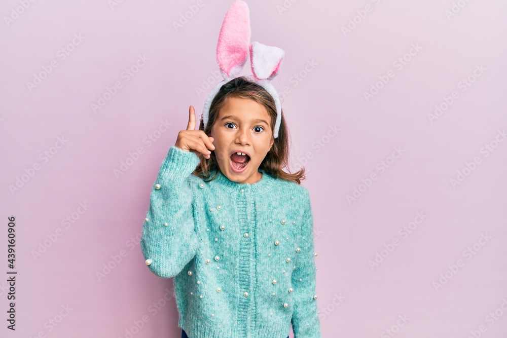 Little beautiful girl wearing cute easter bunny ears pointing finger up with successful idea. exited and happy. number one.