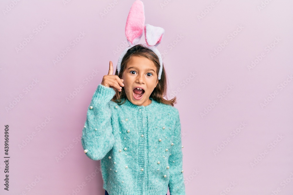 Little beautiful girl wearing cute easter bunny ears pointing finger up with successful idea. exited and happy. number one. Little beautiful girl wearing cute easter bunny ears pointing finger up with successful idea. exited and happy. number one.