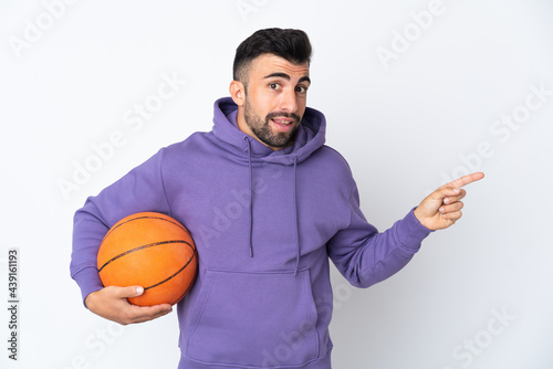 Man playing basketball over isolated white wall pointing finger to the side