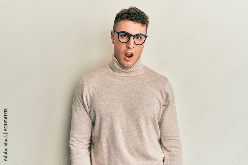 Hispanic young man wearing casual turtleneck sweater in shock face, looking skeptical and sarcastic, surprised with open mouth Hispanic young man wearing casual turtleneck sweater in shock face, looking skeptical and sarcastic, surprised with open mouth