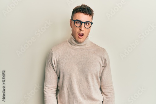 Hispanic young man wearing casual turtleneck sweater in shock face, looking skeptical and sarcastic, surprised with open mouth © Krakenimages.com