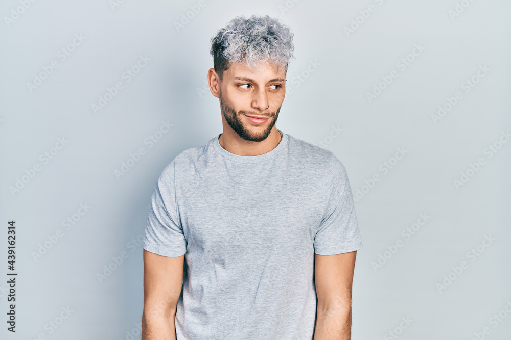 Young hispanic man with modern dyed hair wearing casual grey t shirt smiling looking to the side and staring away thinking. Young hispanic man with modern dyed hair wearing casual grey t shirt smiling looking to the side and staring away thinking.