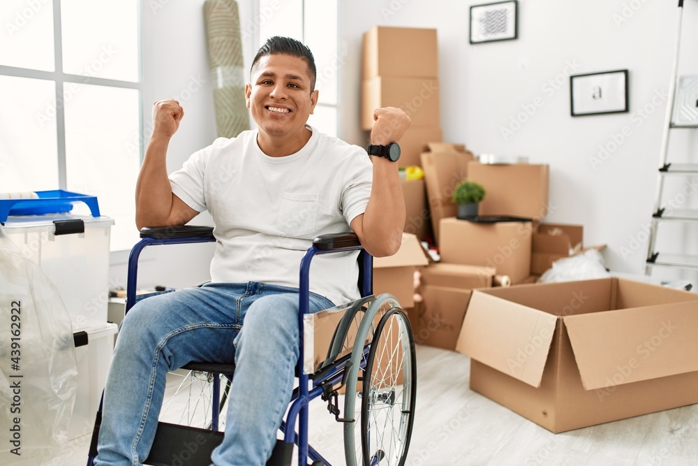 Young hispanic man sitting on wheelchair at new house screaming proud, celebrating victory and success very excited with raised arms Young hispanic man sitting on wheelchair at new house screaming proud, celebrating victory and success very excited with raised arms