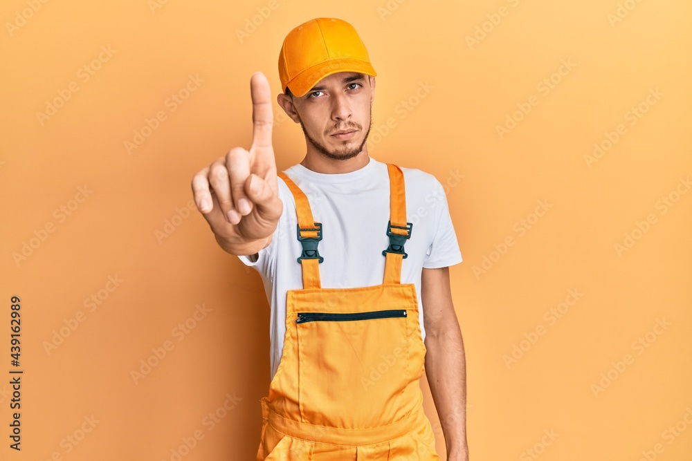 Hispanic young man wearing handyman uniform pointing with finger up and angry expression, showing no gesture Hispanic young man wearing handyman uniform pointing with finger up and angry expression, showing no gesture