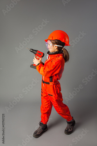 The little girl dressed in a red engineering uniform is holding a screwdriver © oksix