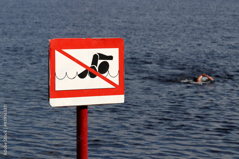 No swimming sign on background of sea and swimmer. Beach holiday on summer sea or river