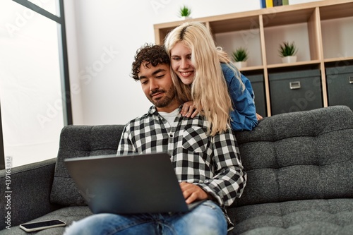 Young couple using laptop sitting on the sofa at home.