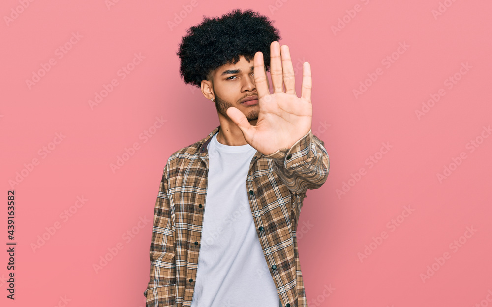 Young african american man with afro hair wearing casual clothes doing stop sing with palm of the hand. warning expression with negative and serious gesture on the face.