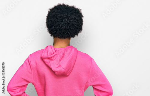 Young african american man with afro hair wearing casual pink sweatshirt standing backwards looking away with arms on body