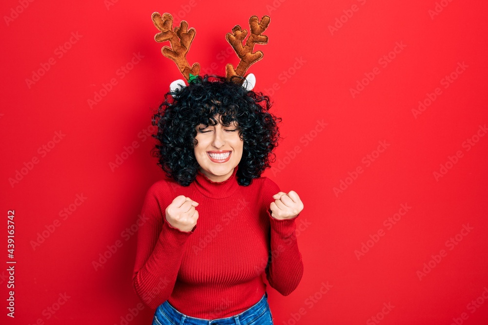 Young middle east woman wearing cute christmas reindeer horns excited for success with arms raised and eyes closed celebrating victory smiling. winner concept. Young middle east woman wearing cute christmas reindeer horns excited for success with arms raised and eyes closed celebrating victory smiling. winner concept.