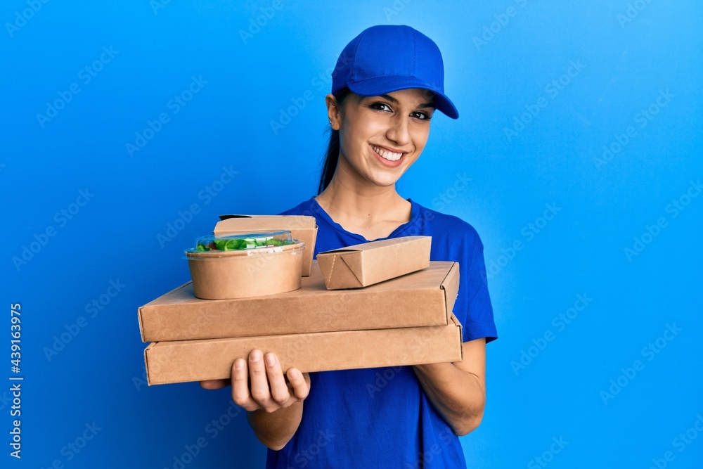 Young hispanic woman holding take away food looking positive and happy standing and smiling with a confident smile showing teeth Young hispanic woman holding take away food looking positive and happy standing and smiling with a confident smile showing teeth