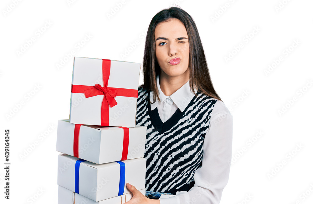 Young brunette teenager holding gifts winking looking at the camera with sexy expression, cheerful and happy face. Young brunette teenager holding gifts winking looking at the camera with sexy expression, cheerful and happy face.