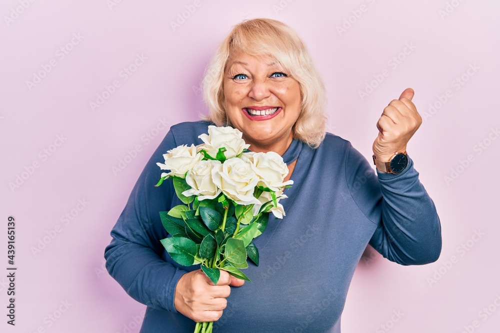 Middle age blonde woman holding flowers screaming proud, celebrating victory and success very excited with raised arm