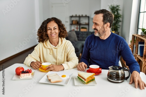 Middle age hispanic couple smiling happy sitting on the table having breakfast at home.