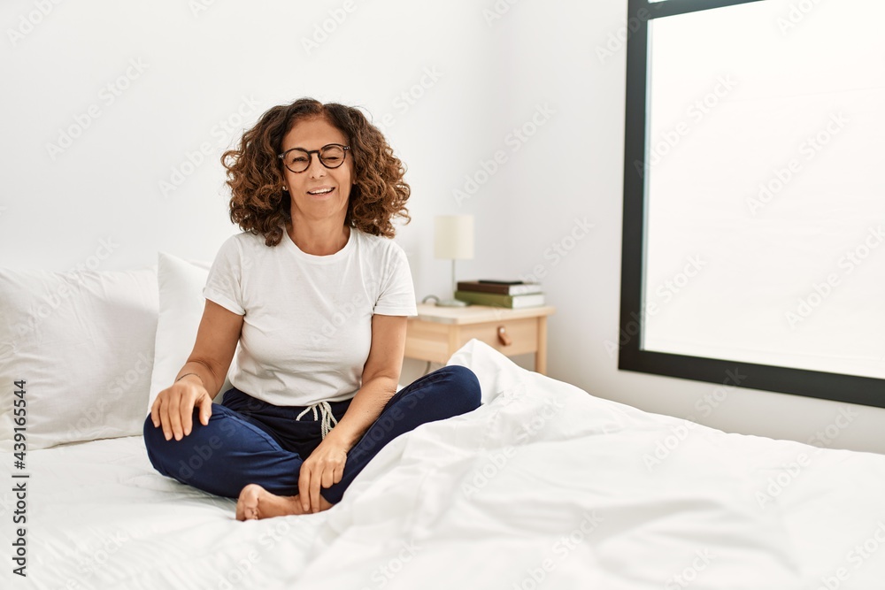 Middle age hispanic woman sitting on the bed at home winking looking at the camera with sexy expression, cheerful and happy face.