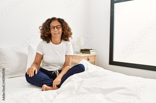 Middle age hispanic woman sitting on the bed at home winking looking at the camera with sexy expression, cheerful and happy face. © Krakenimages.com