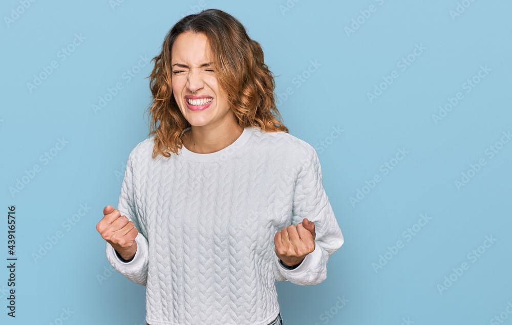 Beautiful young caucasian woman wearing casual winter sweater excited for success with arms raised and eyes closed celebrating victory smiling. winner concept. Beautiful young caucasian woman wearing casual winter sweater excited for success with arms raised and eyes closed celebrating victory smiling. winner concept.