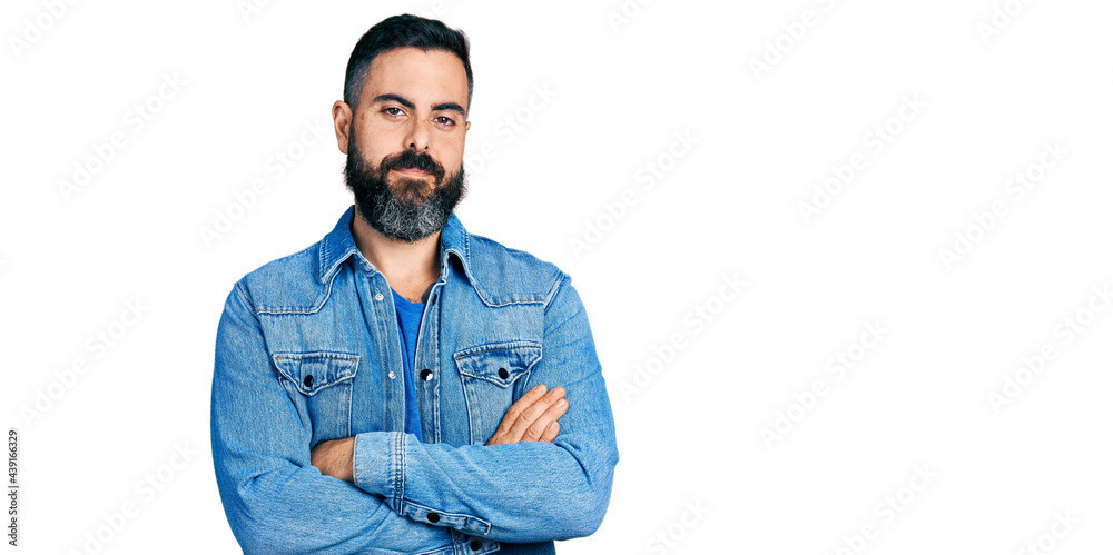 Hispanic man with beard wearing casual denim jacket happy face smiling with crossed arms looking at the camera. positive person. Hispanic man with beard wearing casual denim jacket happy face smiling with crossed arms looking at the camera. positive person.