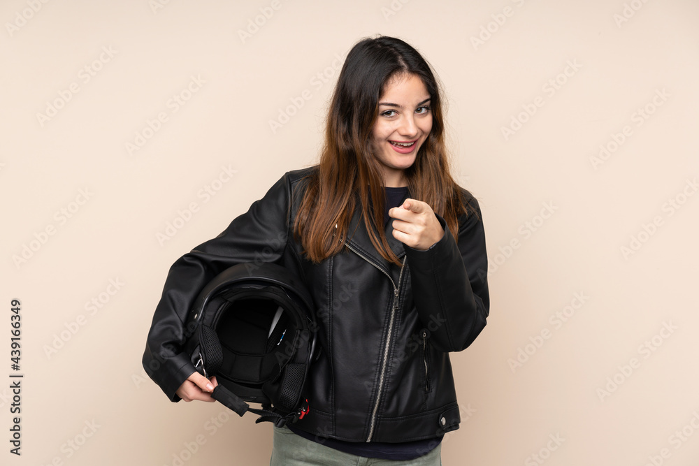 Woman with a motorcycle helmet isolated on beige background points finger at you Woman with a motorcycle helmet isolated on beige background points finger at you