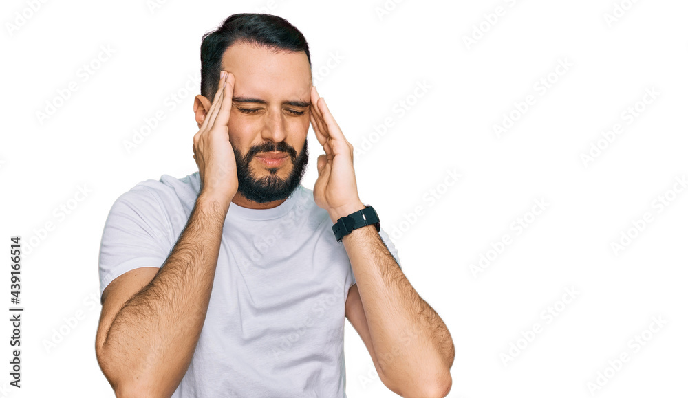 Young man with beard wearing casual white t shirt with hand on head, headache because stress. suffering migraine. Young man with beard wearing casual white t shirt with hand on head, headache because stress. suffering migraine.