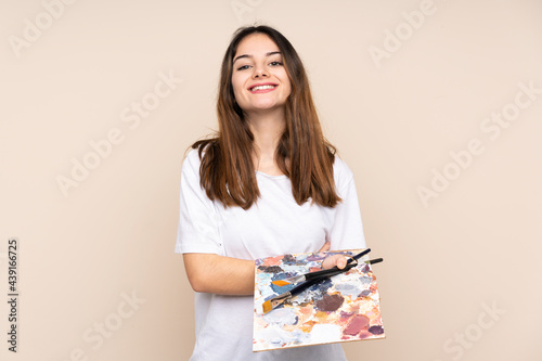 Young artist man holding a palette isolated on beige background laughing