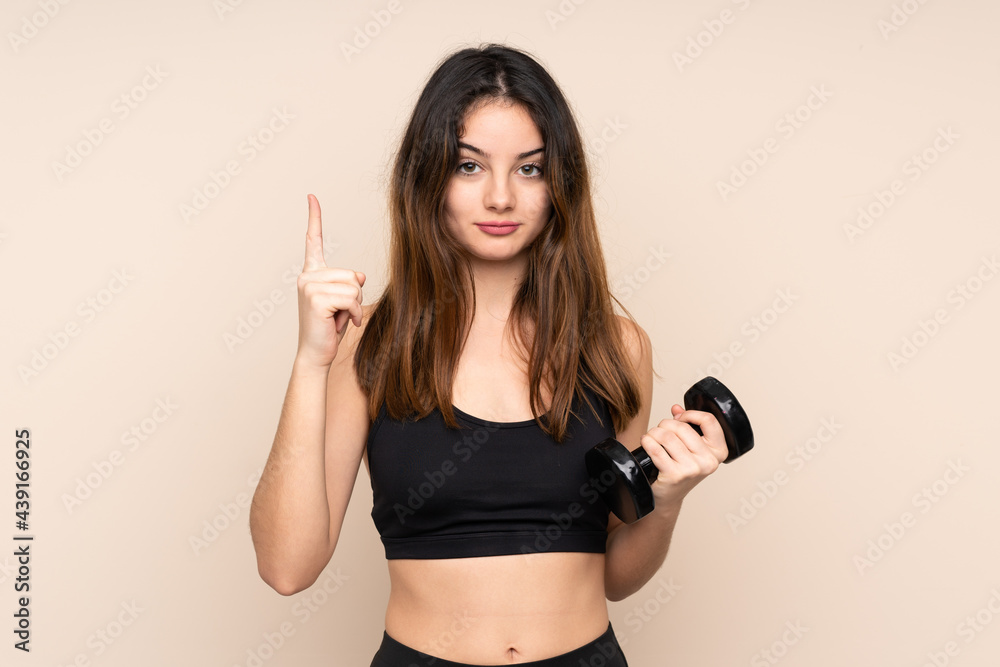 Young sport woman making weightlifting isolated on beige background pointing with the index finger a great idea Young sport woman making weightlifting isolated on beige background pointing with the index finger a great idea