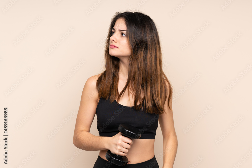 Young sport woman making weightlifting isolated on beige background standing and looking to the side