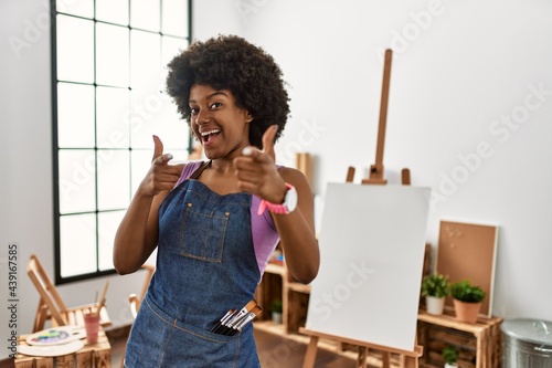 Young african american woman with afro hair at art studio pointing fingers to camera with happy and funny face. good energy and vibes.