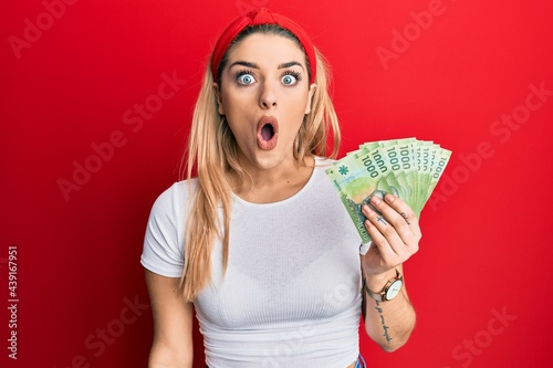 Young caucasian woman holding 1000 chilean pesos scared and amazed with open mouth for surprise, disbelief face photo
