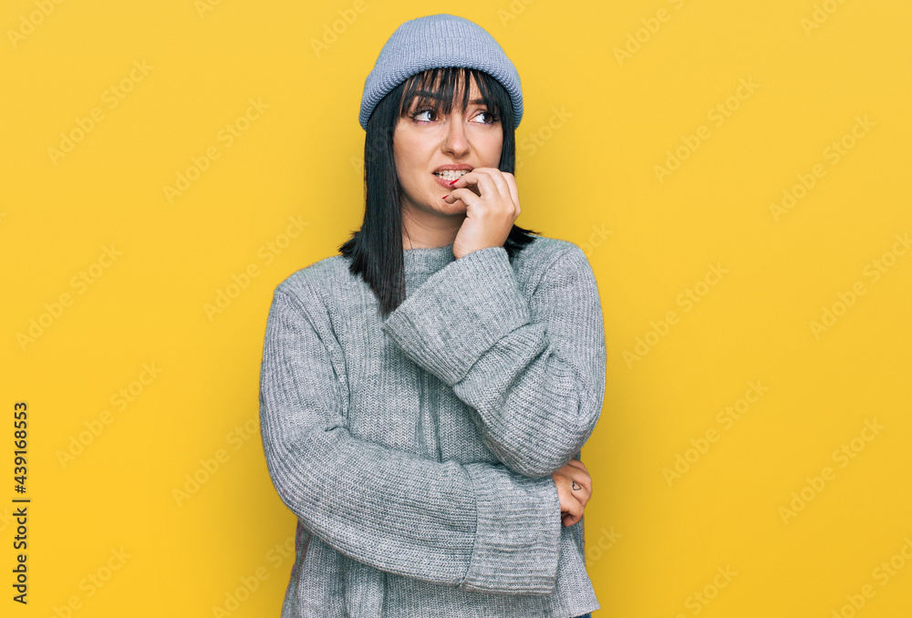 Young hispanic woman wearing cute wool cap looking stressed and nervous with hands on mouth biting nails. anxiety problem. Young hispanic woman wearing cute wool cap looking stressed and nervous with hands on mouth biting nails. anxiety problem.