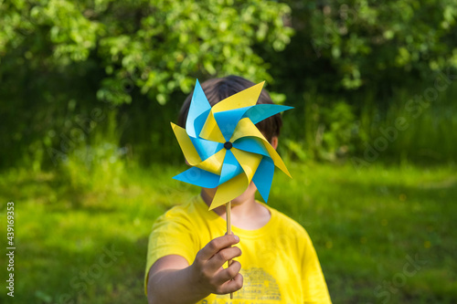 Принти на полотні A boy in a yellow jersey plays with a yellow and blue paper 8-petal weather vane in the garden