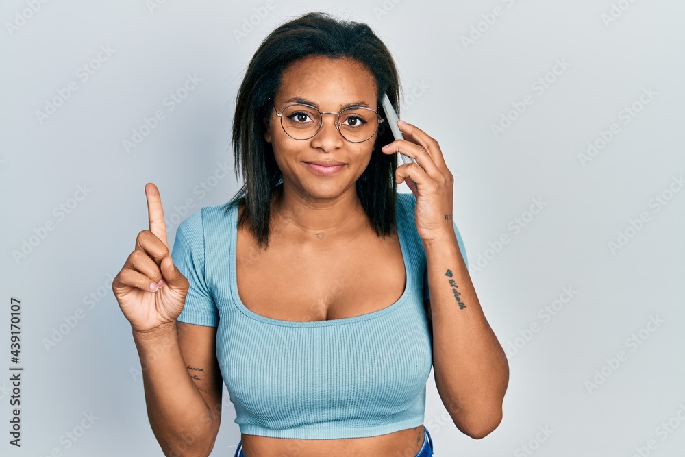 Young african american girl having conversation talking on the smartphone smiling with an idea or question pointing finger with happy face, number one Young african american girl having conversation talking on the smartphone smiling with an idea or question pointing finger with happy face, number one