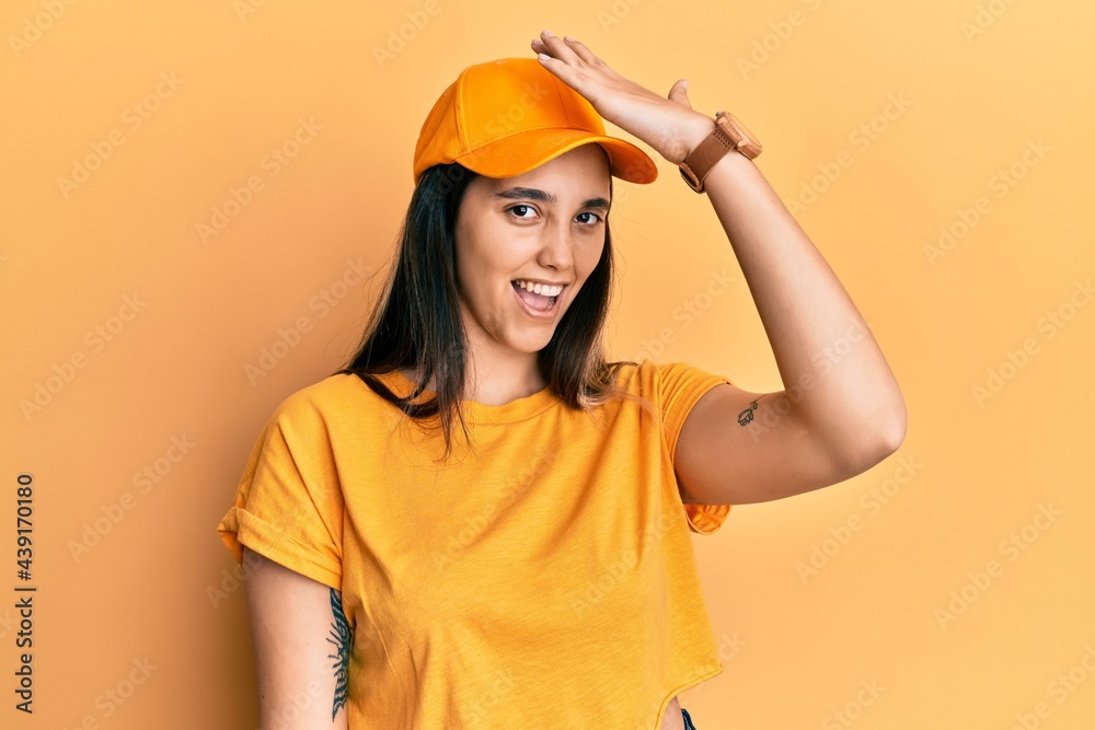 Young hispanic woman wearing delivery uniform and cap surprised with hand on head for mistake, remember error. forgot, bad memory concept.