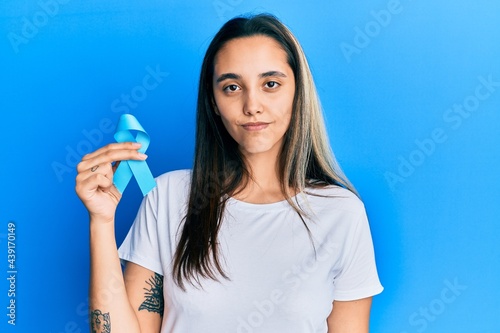 Obraz na plátně Young hispanic woman holding blue ribbon thinking attitude and sober expression