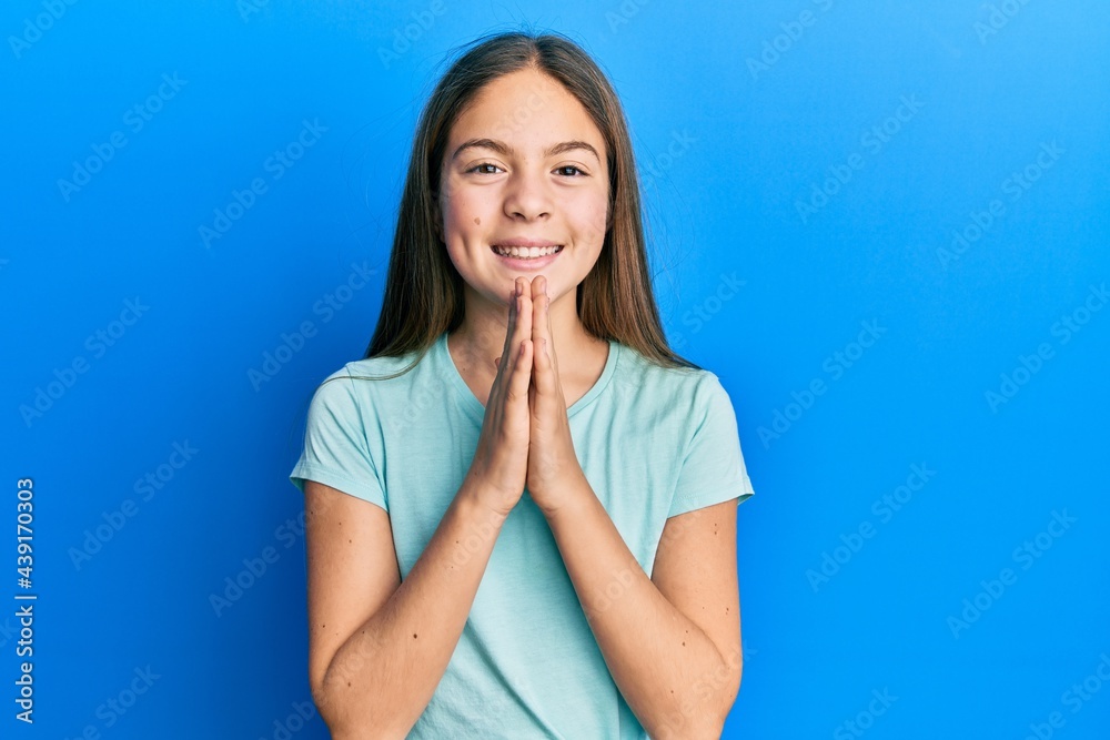 Beautiful brunette little girl wearing casual white t shirt praying with hands together asking for forgiveness smiling confident.