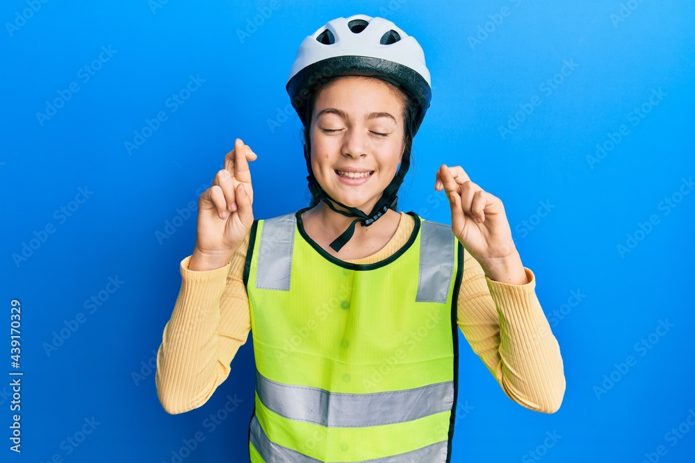 Beautiful brunette little girl wearing bike helmet and reflective vest gesturing finger crossed smiling with hope and eyes closed. luck and superstitious concept. Beautiful brunette little girl wearing bike helmet and reflective vest gesturing finger crossed smiling with hope and eyes closed. luck and superstitious concept.