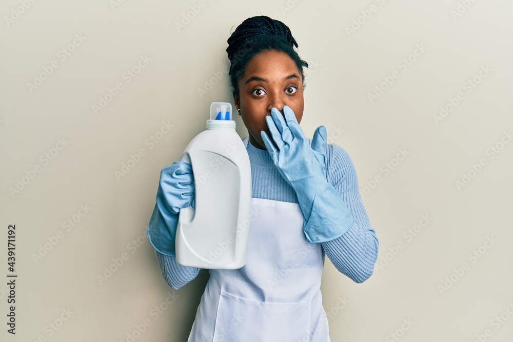 African american woman with braided hair holding detergent bottle covering mouth with hand, shocked and afraid for mistake. surprised expression African american woman with braided hair holding detergent bottle covering mouth with hand, shocked and afraid for mistake. surprised expression