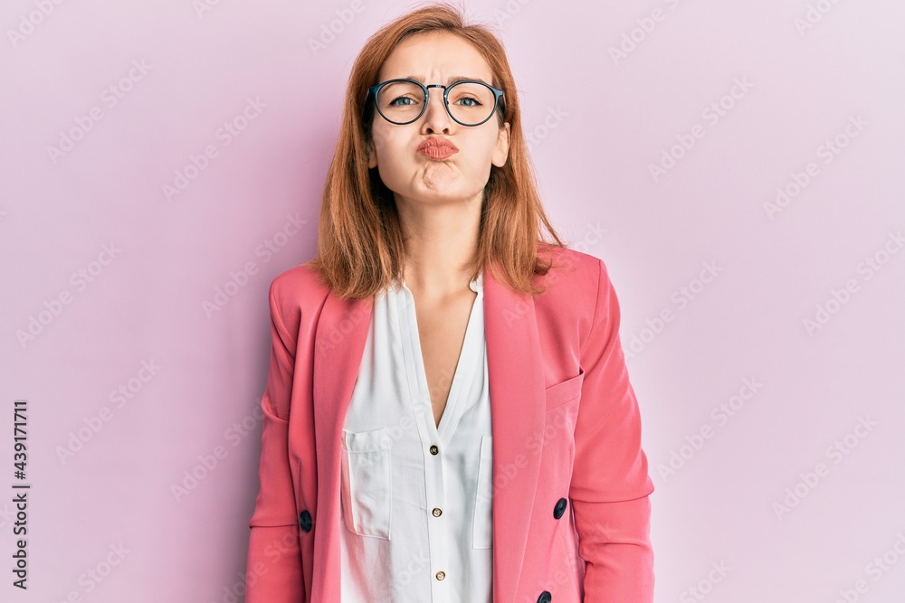 Young caucasian woman wearing business style and glasses puffing cheeks with funny face. mouth inflated with air, crazy expression. Young caucasian woman wearing business style and glasses puffing cheeks with funny face. mouth inflated with air, crazy expression.