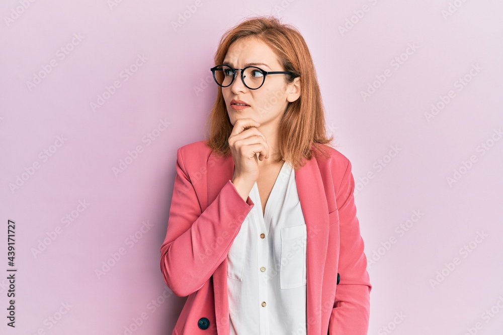 Young caucasian woman wearing business style and glasses with hand on chin thinking about question, pensive expression. smiling with thoughtful face. doubt concept.
