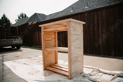 Unfinished wooden stereo storage table sitting on a tarp in the driveway awaiting painting