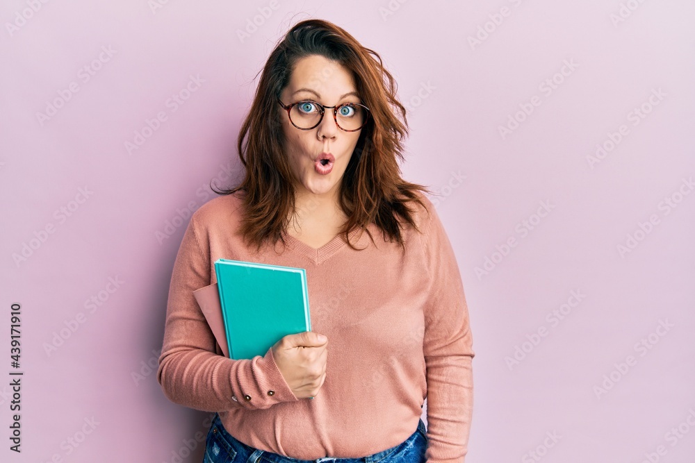 Young caucasian woman holding book scared and amazed with open mouth for surprise, disbelief face Young caucasian woman holding book scared and amazed with open mouth for surprise, disbelief face