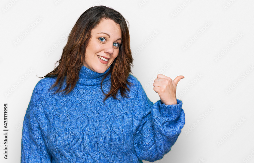 Young plus size woman wearing casual clothes smiling with happy face looking and pointing to the side with thumb up. Young plus size woman wearing casual clothes smiling with happy face looking and pointing to the side with thumb up.