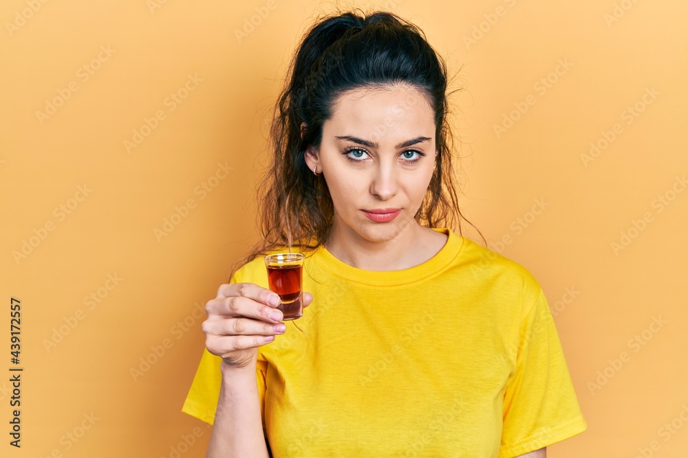 Young hispanic woman drinking whiskey shot thinking attitude and sober expression looking self confident