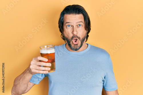 Middle age caucasian man drinking a pint of beer scared and amazed with open mouth for surprise, disbelief face